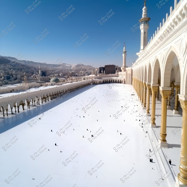 Image showing the courtyard of the Grand Mosque in Mecca, Saudi Arabia, with a row of gold and white columns on the right and tall minarets in the background. Several individuals in traditional clothing are scattered across the wide white floor of the courtyard. Some buildings and distant mountains are visible under the clear blue sky.