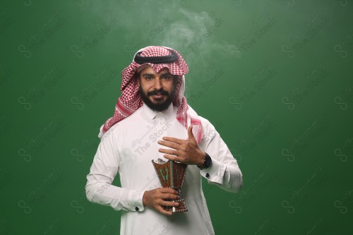 بورتريه رجل سعودي يرتدي الزي السعودي التقليدي يحمل المبخرة ويتطيب بالبخور