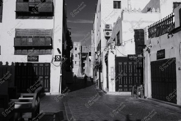 Black and white image of a narrow street in a historic area with traditional buildings and signs on the doors.