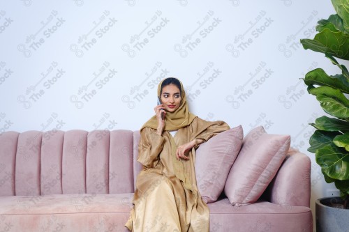 A Saudi girl sitting on the sofa and making different expressions using a mobile phone