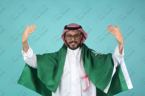 شاب سعودي يرتدي الزي السعودي يلوح بيدية وحمل علم السعودية على خلفية سماوية ويظهر تعابير الفرح ، كأس العالم.