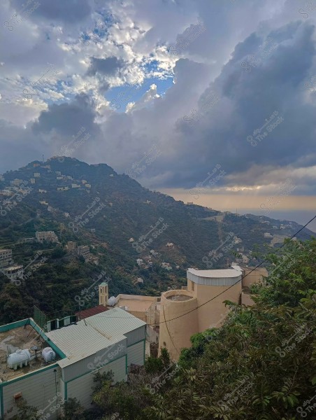 منظر طبيعي لمنطقة جبلية مع منازل متناثرة تحت غيوم كثيفة في السماء.