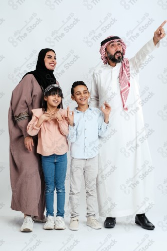 Portrait of a Saudi family looking towards a place, two children standing next to their parents pointing towards a goal, signs of happiness, a happy family atmosphere, the concept of a happy family, spending enjoyable family times