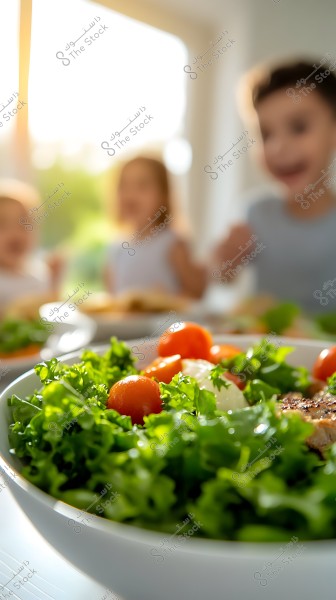 An image of a fresh salad with cherry tomatoes and lettuce in a white bowl, with a blurred background of children sitting around a table in a naturally lit room. Sunlight is coming through a window in the background.
