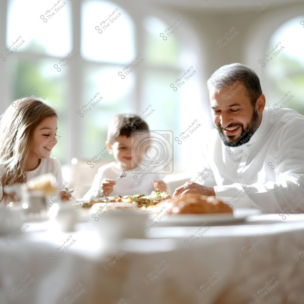 An image of a family of three sitting around a dining table. The father, with a beard, is wearing a traditional white robe and is smiling. A young girl and boy sit beside him, each holding utensils, appearing to enjoy the meal. The background is bright with large windows.