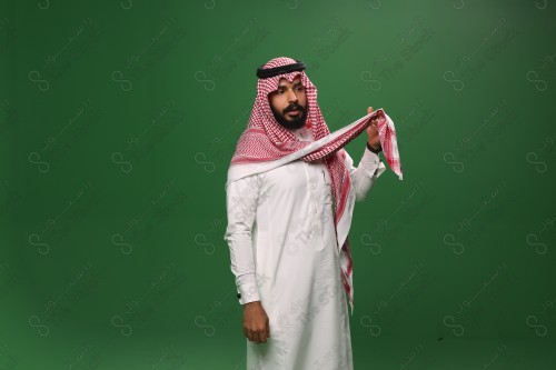 رجل سعودي يقف على خلفية خضراء يرتدي الثوب و الشماغ، يمسك الشماغ ويقوم بتعديله ، احتفالات العيد