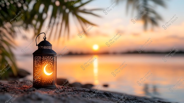 A warmly lit lantern sits on the shore during sunset. The lantern features intricate patterns including a crescent moon symbol. In the background, the sun’s rays glimmer over the water, with palm leaves appearing blurred in the foreground.