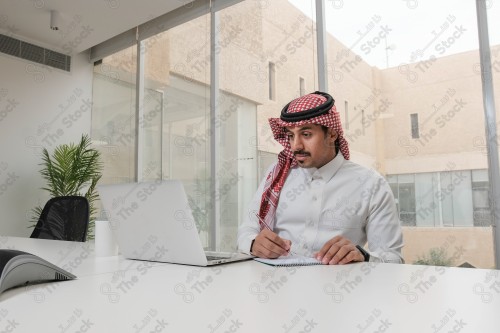 A Saudi man wearing the Saudi thobe sits in the meeting room and uses the mobile device