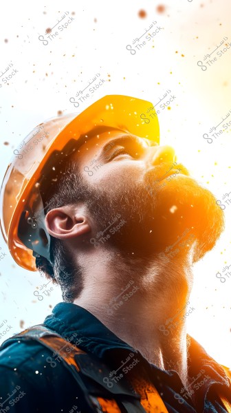 A portrait of a man wearing a yellow safety helmet looking upwards. There is bright light behind him and visual effects resemble particles scattered in the air. He is wearing a dark work jacket. His facial expression shows focus and determination.