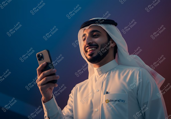 Image of a man wearing traditional Gulf attire, including a white and black headscarf, looking at his phone with a smile. The background is a calm blue, creating a modern and relaxed atmosphere.