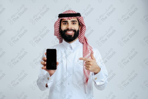 رجل سعودي يرتدي الزي الرسمي التقليدي على خلفية بيضاء, تصفح الهاتف المحمول, دردشه ومحادثات, التواصل مع الأصدقاء, مكالمات فيديو, القراءه من الهاتف المحمول, قضاء وقت ممتع وهادئ, تسليه وترفيه.