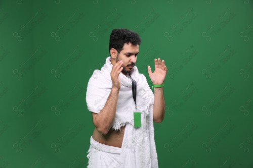 Portrait of a Saudi pilgrim on a green background wearing the Ihram to perform the Hajj rituals during prayer in several directions