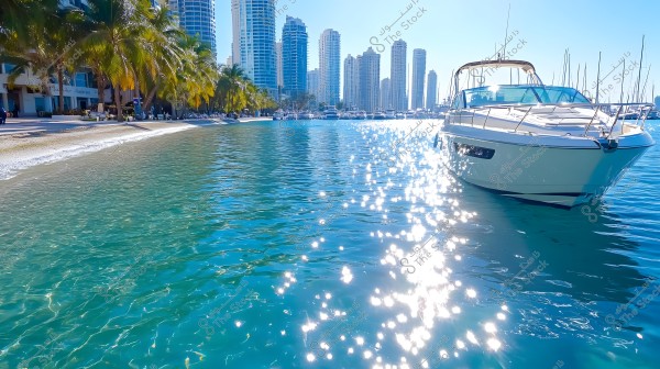 Scenic view of a waterfront under bright sunlight, featuring a luxury boat in the foreground. Skyscraper towers are visible in the background, alongside palm trees lining the sandy beach. The sky is clear blue, and the water sparkles with reflected light.