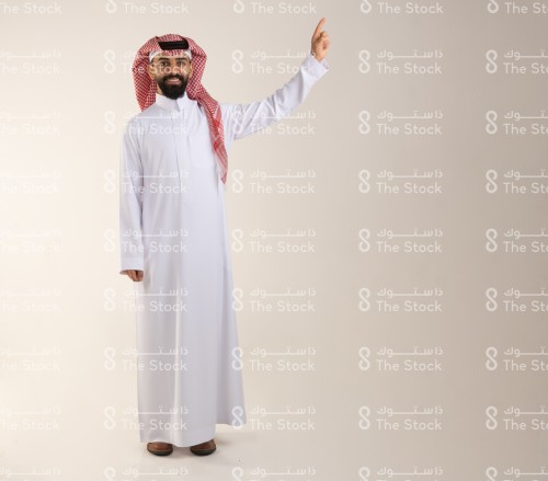 شاب سعودي يرتدي الزي السعودي التقليدي يشير بإصبعه السبابة يسار الصورة، رجل سعودي ينقر على أيقونة افتراضية