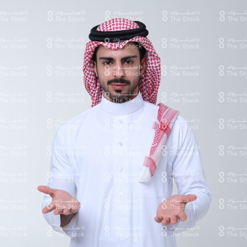 بورتريه رجل سعودي يرتدي الثوب ويقف أمام خلفية بيضاء، يتفاعل بحركات تعبيرية بيديه