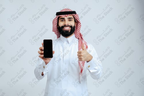 رجل سعودي يرتدي الزي الرسمي التقليدي على خلفية بيضاء, تصفح الهاتف المحمول, دردشه ومحادثات, التواصل مع الأصدقاء, مكالمات فيديو, القراءه من الهاتف المحمول, قضاء وقت ممتع وهادئ, تسليه وترفيه.