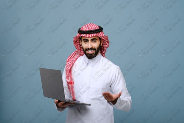 بورتريه شاب سعودي يرتدي الزي السعودي يحمل جهاز المحمول وتظهر على ملامحة السعادة ، يقف على خلفية سماوية