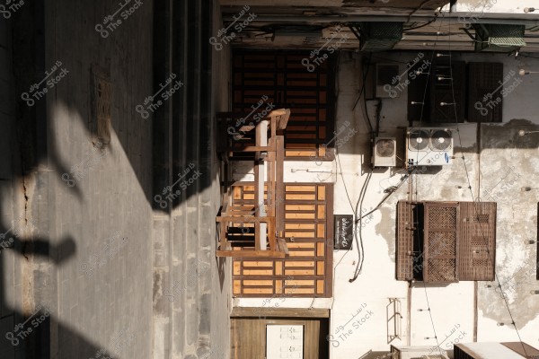 An urban area image featuring a large wooden door and an air conditioning unit mounted on the wall. The traditional architectural design is evident with shadows cast on the wall.