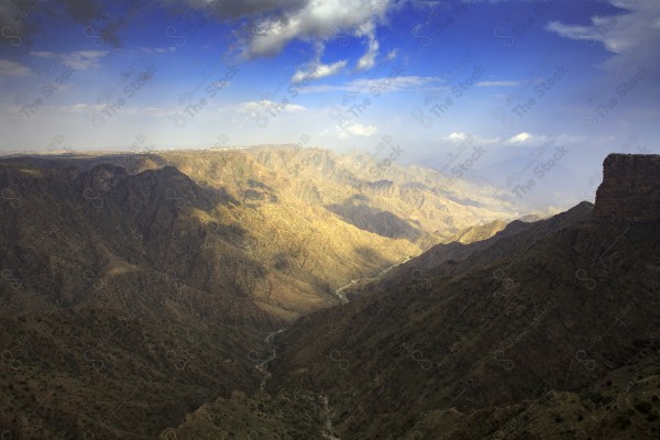 Aerial shot of a series of rocky mountains and the overlapping of clouds between them, nature in Saudi Arabia, the sky is clear