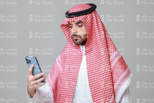 شاب سعودي يرتدي الزي السعودي التقليدي يستخدم الجوال، رجل يتصفح هاتفه المحمول