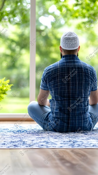 An image of a man sitting from behind on a blue prayer rug in a well-lit room overlooking a green garden. The man is wearing a blue plaid shirt and a white knitted cap. The scene conveys a sense of meditation and tranquility.