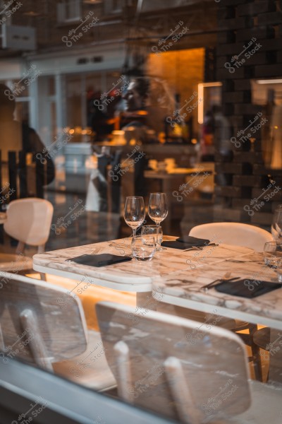 A table in a fancy restaurant set for dinner, with wine glasses and tableware, seen through a glass window.