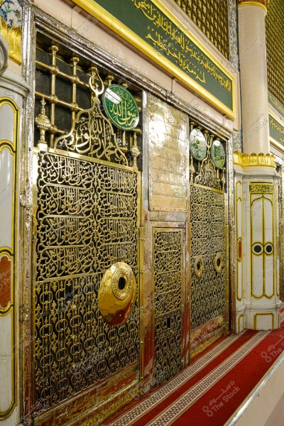 The image shows the facade of the Prophet\'s chamber in Al-Masjid an-Nabawi in Medina. The design features intricate Islamic calligraphy in golden Arabic script on an ornate metal grille. The mosaic is finely colored and decorates the area around the tomb. The upper panels contain religious texts written in Arabic script on a green background.