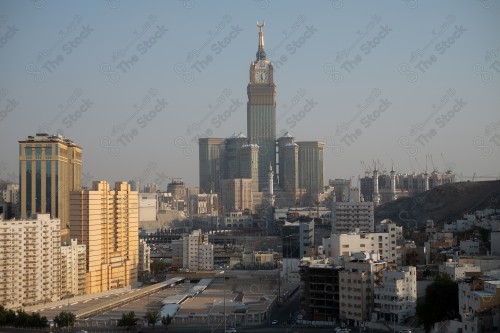 صورة لبرج الساعة وقت الغروب في مكة المكرمة، وتحيط بها مباني ومعالم المدينة.