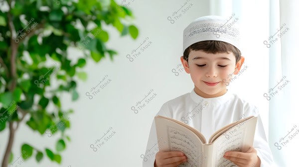 The image shows a child wearing a traditional white thobe and cap, reading from a book in Arabic script. The background contains green foliage, suggesting a calm indoor or open setting.