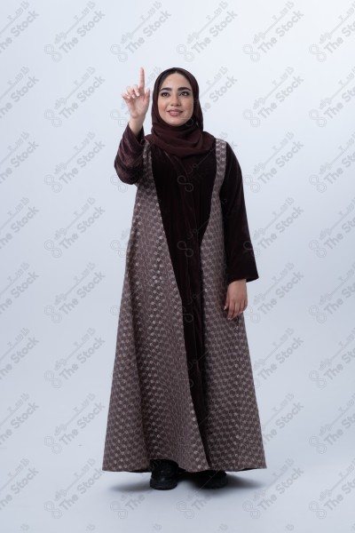 A young joyful Saudi woman wearing an abaya, raising her finger. Standing on white background.