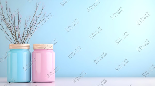 Two large jars with wooden lids are placed on a white surface. The jar on the left is blue and contains thin, dried plant stems. The jar on the right is pink. The background is light blue.
