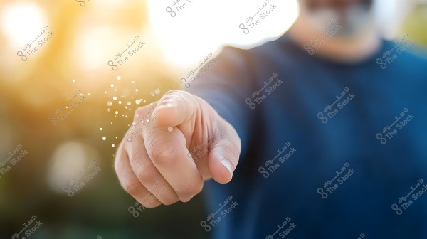 An image showing a person\'s hand reaching toward the camera, with indistinct clothing in the background. The hand is extended with the index finger pointing forward. The background is blurred, featuring some warm lights.