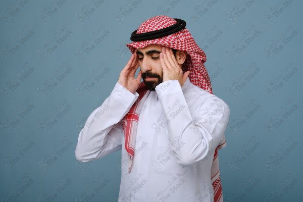 بورتريه شاب سعودي يرتدي الزي السعودي على خلفية سماوية، يمسك رأسه ، يشعر بالصداع ،آلام الصداع والمرض