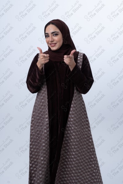 A young happy Saudi woman wearing an abaya, pointing her finger. Standing on white background.