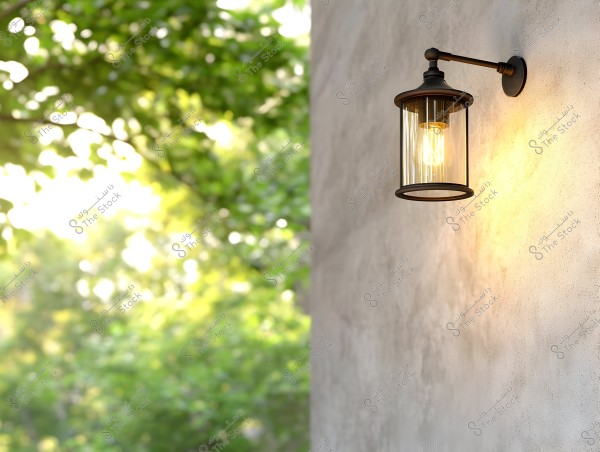 An outdoor wall-mounted lamp with a classic design attached to a grey concrete wall, glowing with warm light. In the background, there is a natural view of green plants illuminated by sunlight, creating a calm and verdant atmosphere.