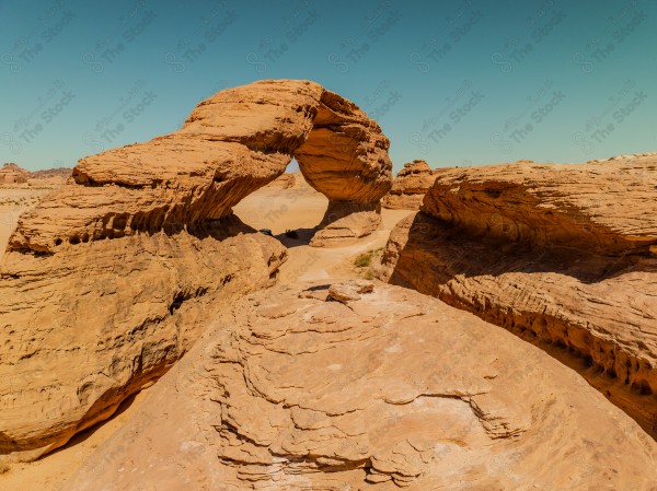 A natural sandstone arch in a desert landscape under a clear blue sky.