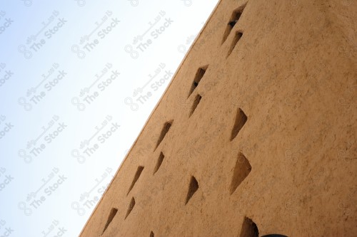 A heritage wall built of mud with a set of holes in the middle, and the sky is clear during the day