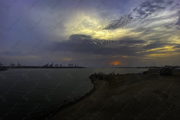 A snapshot of a group of people fishing at sunset, and the sky appears orange in Jeddah, buildings and landmarks, rivers and seas.