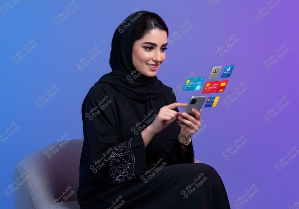 Image of a woman sitting and wearing a black abaya and hijab, pointing at a smartphone. Floating virtual cards are displayed next to the phone, suggesting interaction with banking apps or electronic services. The background is a gradient of blue and purple.