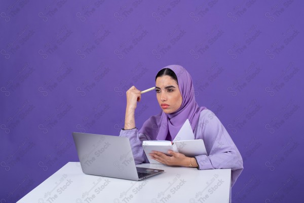 Portrait of a young Saudi woman wearing an abaya and hijab, holding a pen and thinking, against a purple background