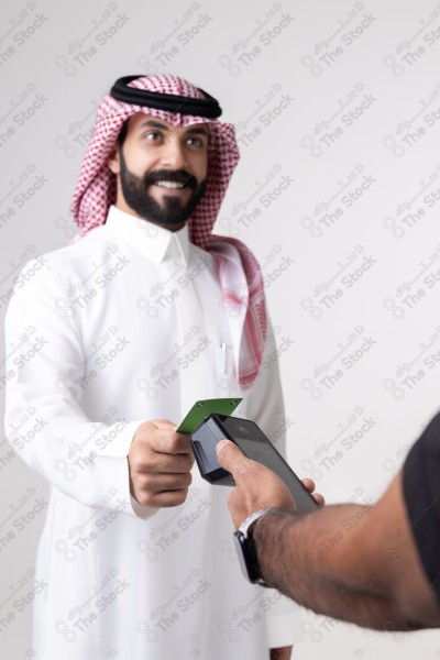 Portrait of a Saudi man holding a card and making automatic payments on a white background