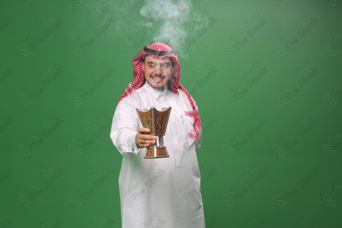 رجل سعودي يرتدي الزي التقليدي على خلفية خضراء ، التطيب بالبخور والعود ، استخدام خشب العود في المناسبات والأعياد.