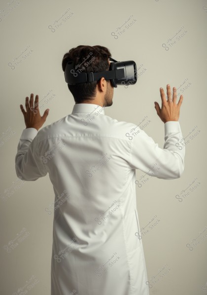 An image of a man wearing virtual reality goggles, viewed from behind, extending his hands forward interactively. The man is wearing a traditional white thobe, suggesting a potential Gulf origin.