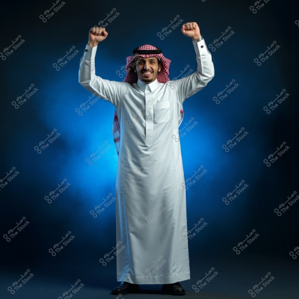 A portrait of a man wearing traditional Saudi attire, consisting of a white thobe and a red shemagh with an agal, standing and smiling with his arms raised in celebration. The dark blue background provides a dramatic effect to the image.