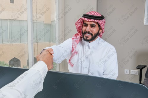 رجلان سعوديان يرتديان الزي السعودي التقليدي يتصافحان أثناء العمل في أروقة المكتب