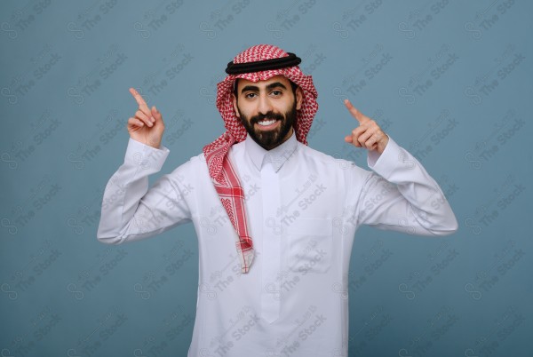 بورتريه شاب سعودي يرتدي الزي السعودي يقوم بالتفاعل بيدية ، ويظهر بتعابير وجه، على خلفية سماويه