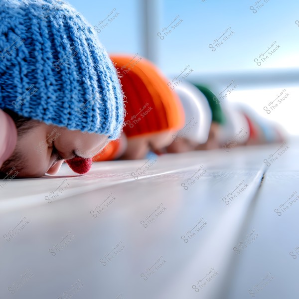 A group of people in a row performing sujud (prostration) on a wooden surface. They are wearing colorful woolen hats in various colors, including blue, orange, white, and green. The image captures the moment from a close angle, highlighting the variety of colors in the hats.