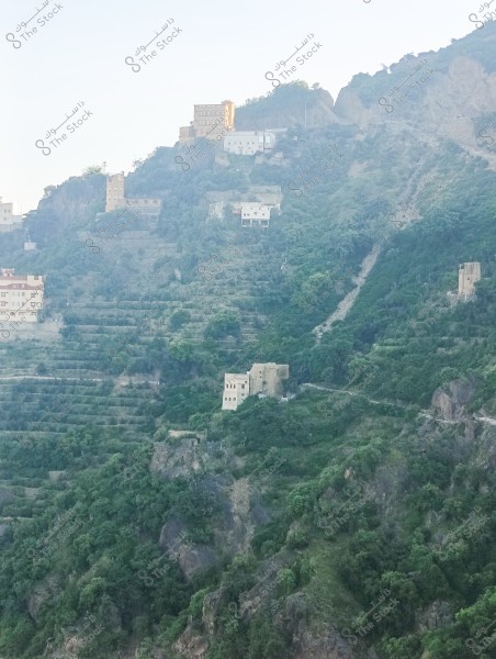 An image showing traditional houses built on the side of a lush, green mountain. The neighborhood is set on agricultural terraces, with multiple homes constructed at various levels of the mountain. Trees and shrubs cover the surrounding area, providing a natural and breathtaking scene. The buildings are made from traditional materials, typical of local architecture in mountainous regions.