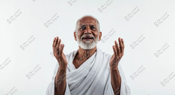 An image of an elderly man wearing a white robe, smiling with his hands slightly raised in front of a white background. The man has a white beard and appears to be in a state of happiness or inner peace.
