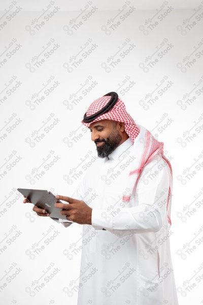 Portrait of a Saudi man holding an iPad in his hand, looking at his screen and making different expressions, white background